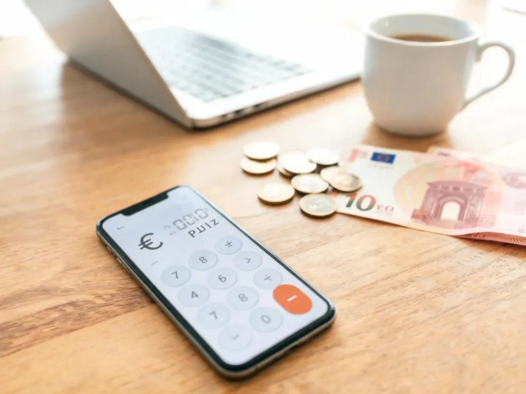Smartfon z kalkulatorem przeliczającym euro na złotówki na biurku, obok monety i banknoty euro w jasnym domowym biurze.